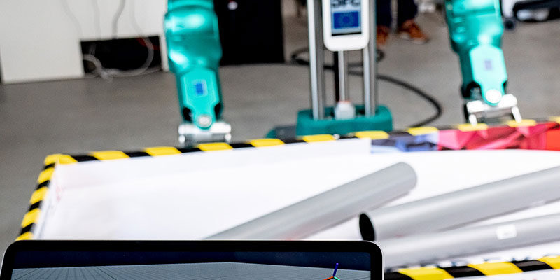 Humanoider Greifroboter des KIT-H2T (Hintergrund) greift kontaminierte Teile autonom aus einer Kiste um sie für die Reinigung vorzubereiten. Auf dem Tablet (Vordergrund) ist der digitaler Zwilling mit der Anzeige des vom Roboter gewählten Griffs zu sehen. Per Tablet kann der Operator bei Bedarf eingreifen. (Foto: ROBDEKON / Fraunhofer-Institut für Optronik, Systemtechnik und Bildauswertung IOSB)