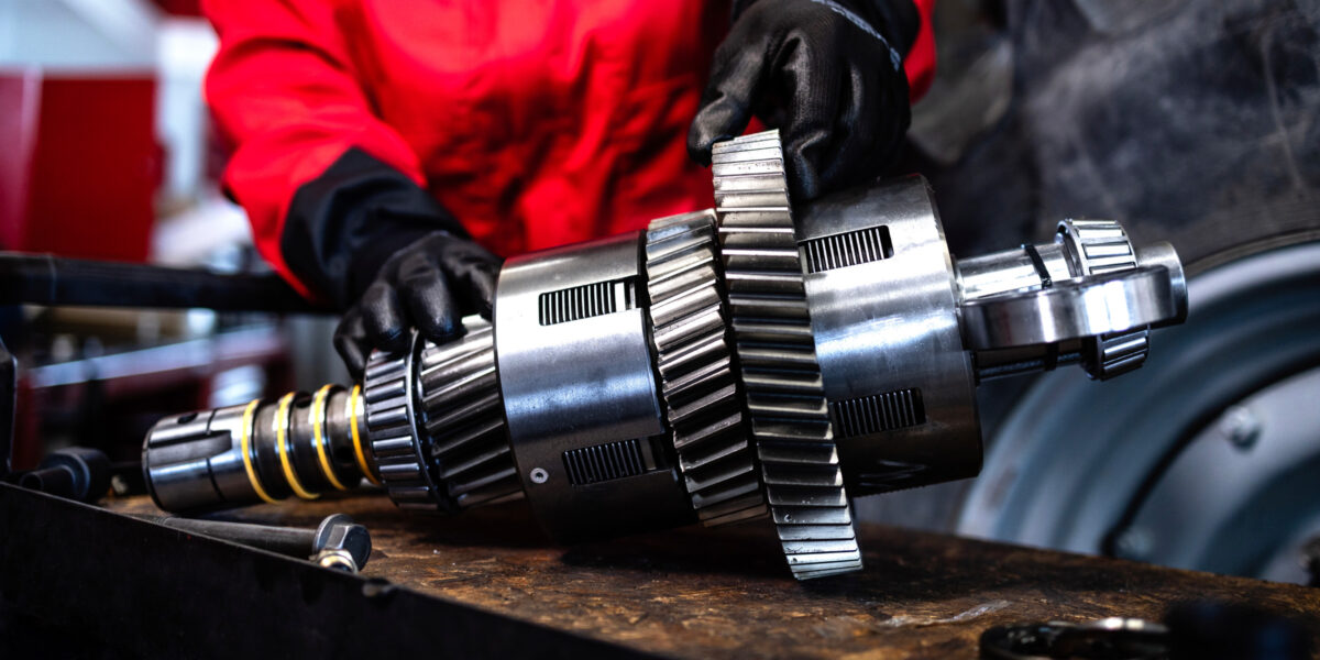 Mechaniker im roten Arbeitsanzug und schwarzen Handschuhen repariert und wartet Getriebe für Traktoren und landwirtschaftliche Maschinen. (Foto: Smederevac (iStock))