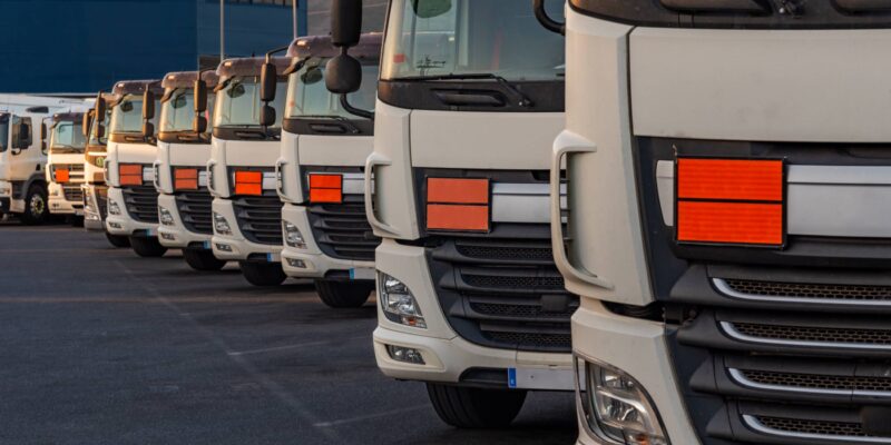 Mehrere LKW in Reihe mit organgefarbenen Tafeln, die auf einen Gefahrguttransort hinweisen (Foto: Miguel Perfectti (iStock))